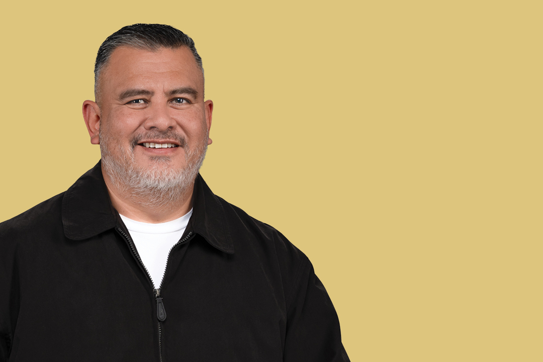 Middle-aged man with short gray hair and beard wearing a black jacket and white shirt, smiling confidently as he embraces successful snoring treatment, against a plain beige background.
